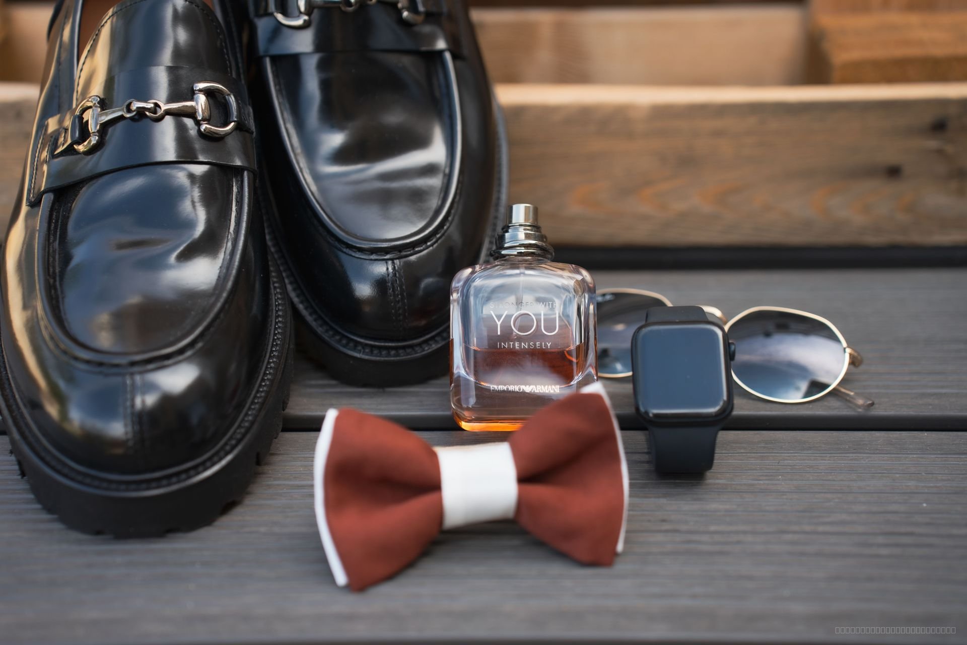 Chaussures noires, nœud papillon bordeaux, montre, lunettes et parfum disposés pour les préparatifs