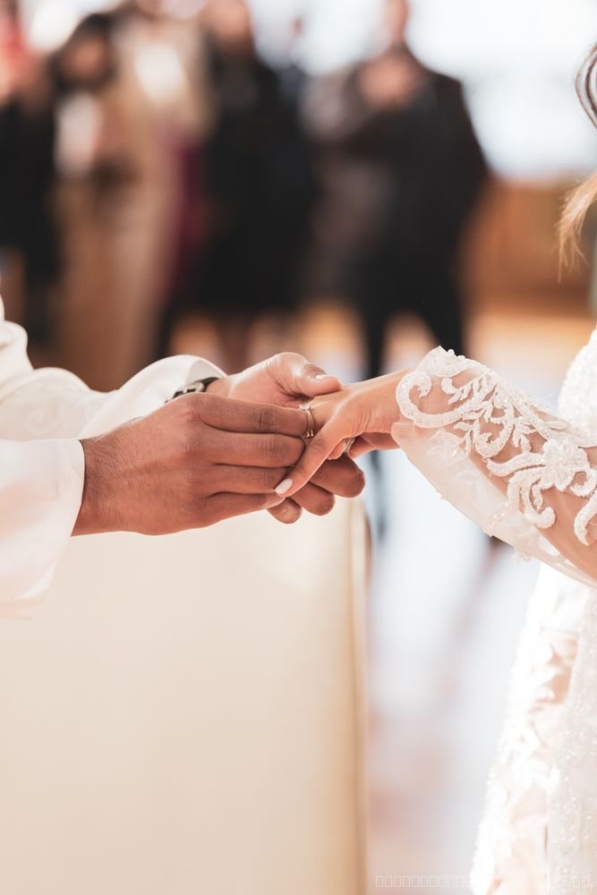 Gros plan sur l’échange des alliances, avec la manche en dentelle de la mariée