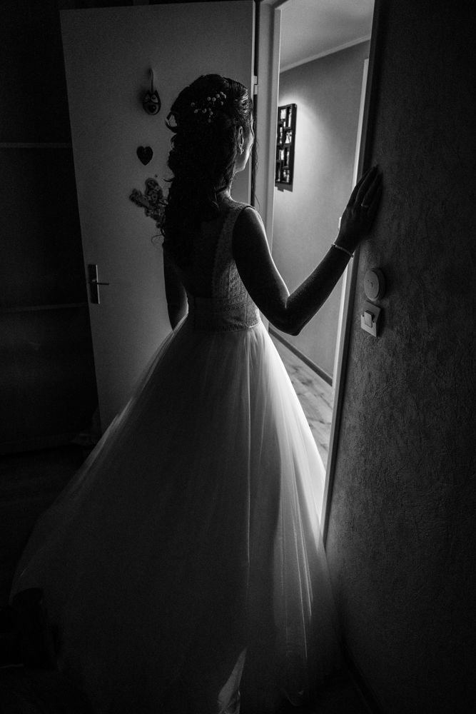 Silhouette de la mariée près d’une porte dans une pièce sombre, en noir et blanc