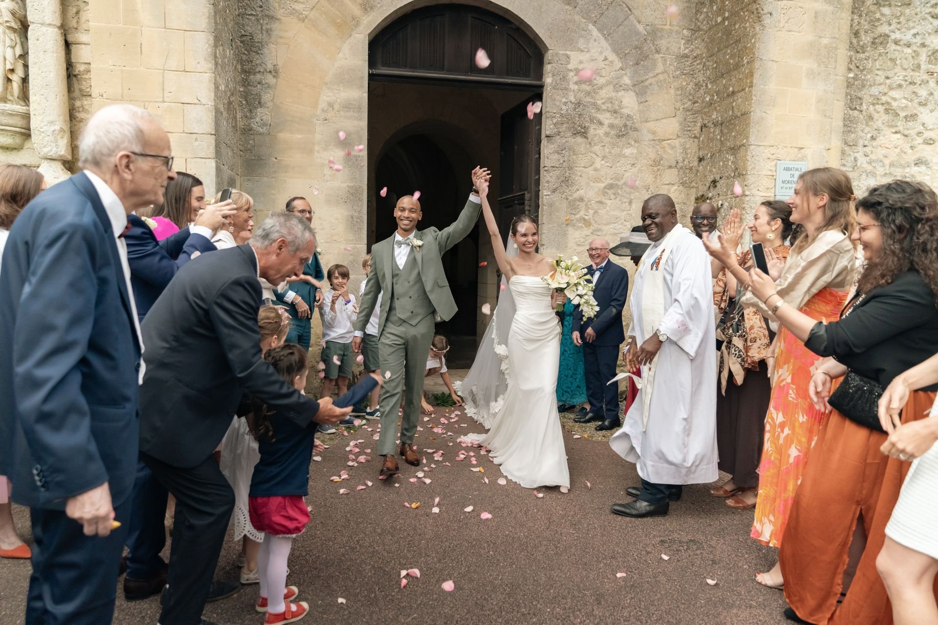 Les mariés sortent d’un édifice en pierre sous les pétales lancés par les invités