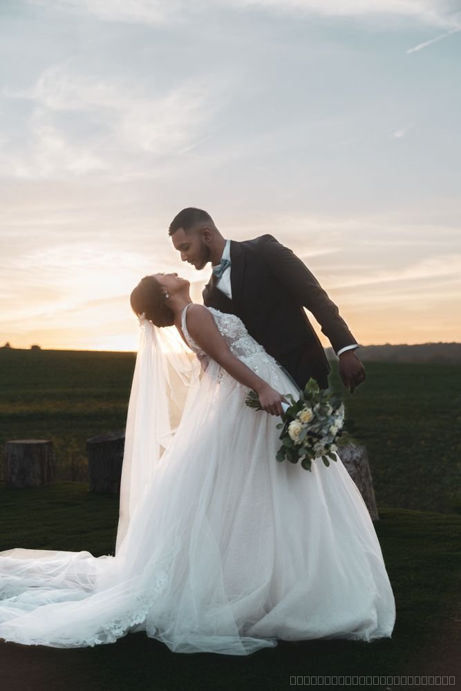 Le marié enlace la mariée penchée en arrière dans un champ au coucher du soleil