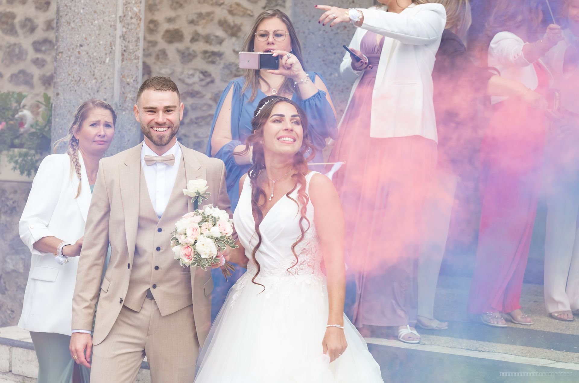 Les mariés entourés de leurs invités dans une fumée rose et bleue
