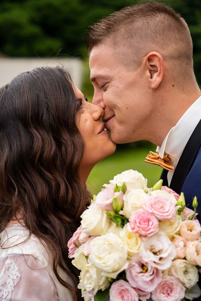 Les mariés s’embrassent derrière un bouquet de roses roses et blanches