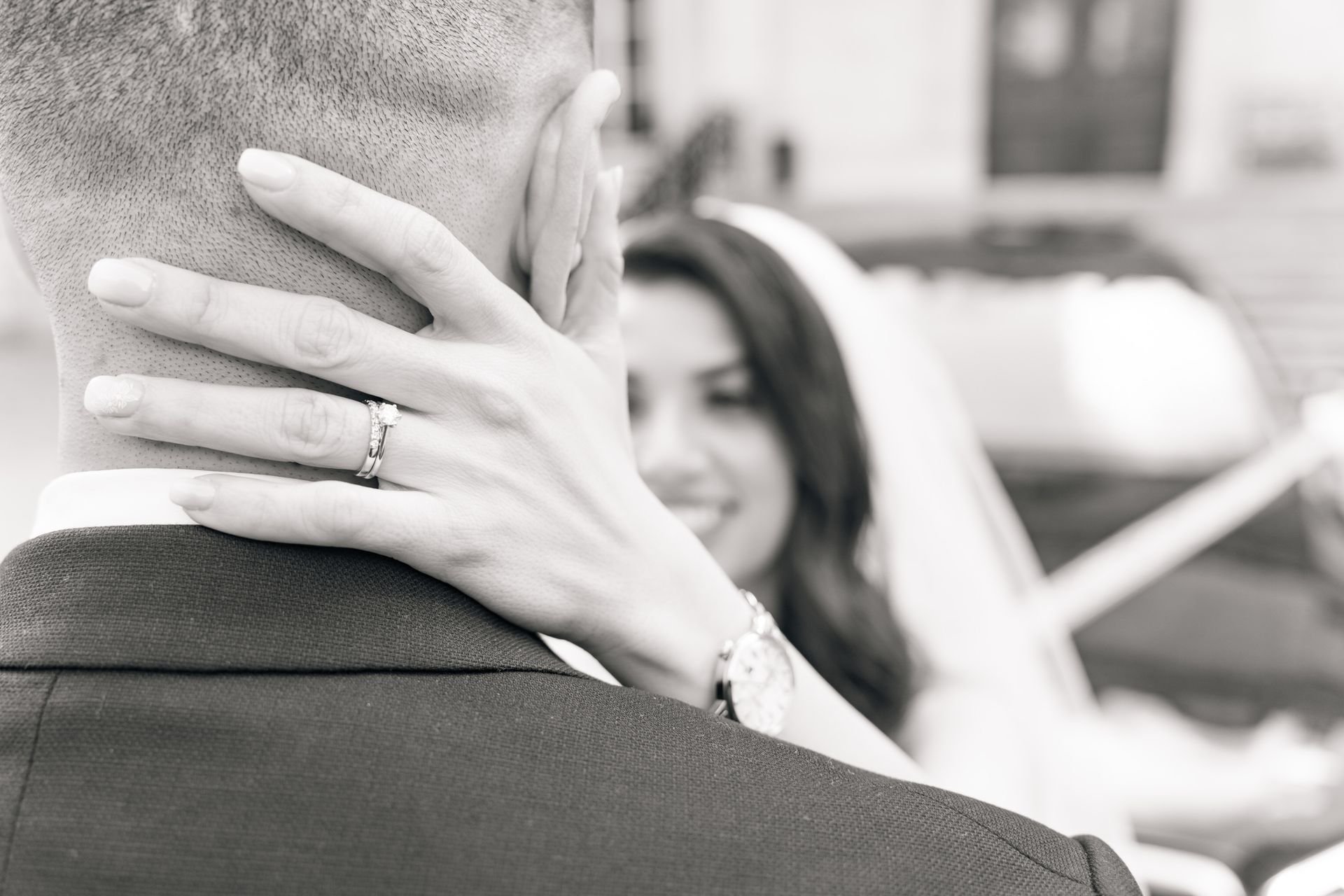 La main de la mariée portant son alliance sur la nuque du marié, en noir et blanc