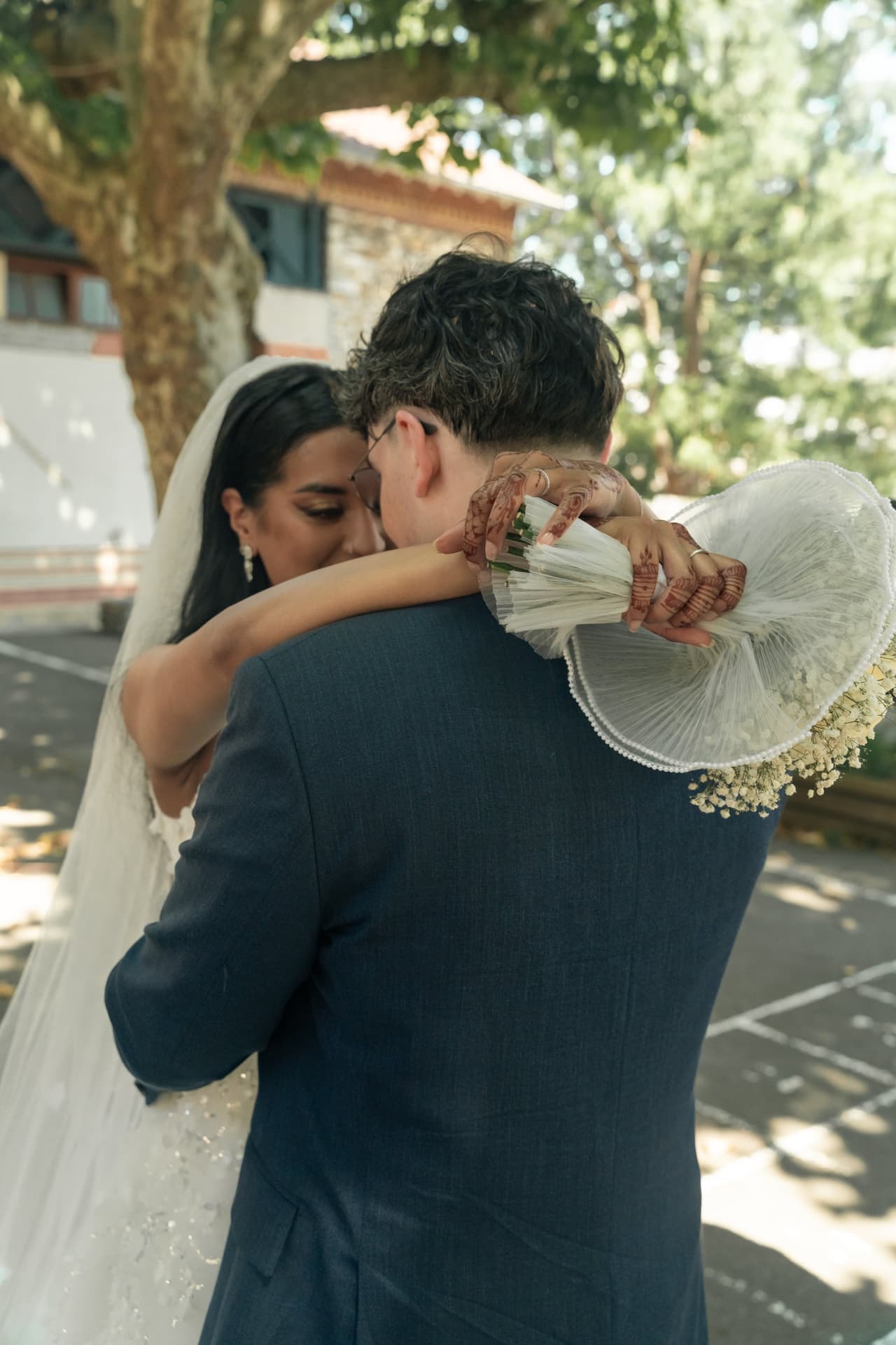 Les mariés s’enlacent sous les arbres, la mariée tenant son bouquet derrière le marié