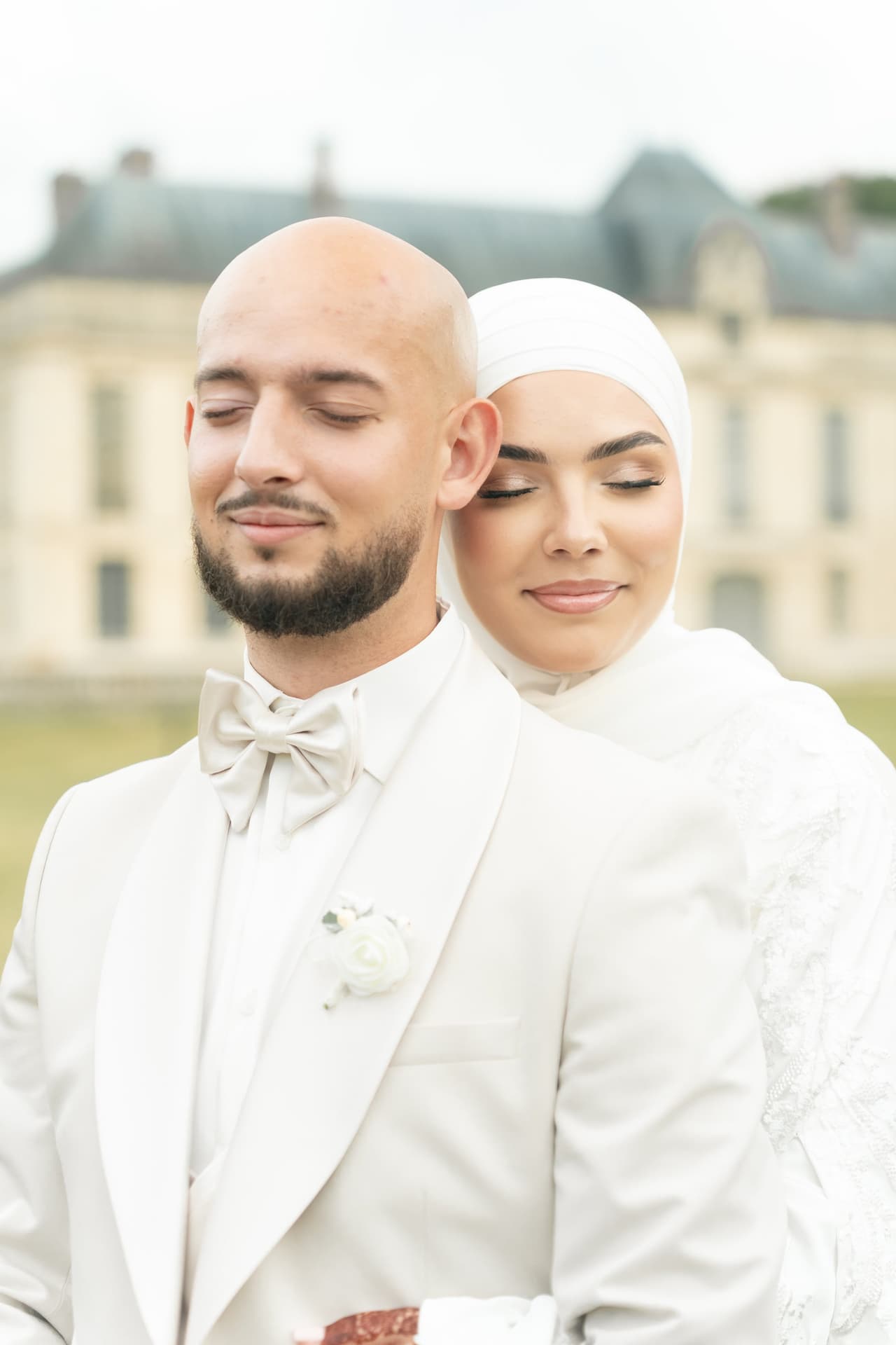 Les mariés en tenues blanches, la mariée enlacée derrière le marié