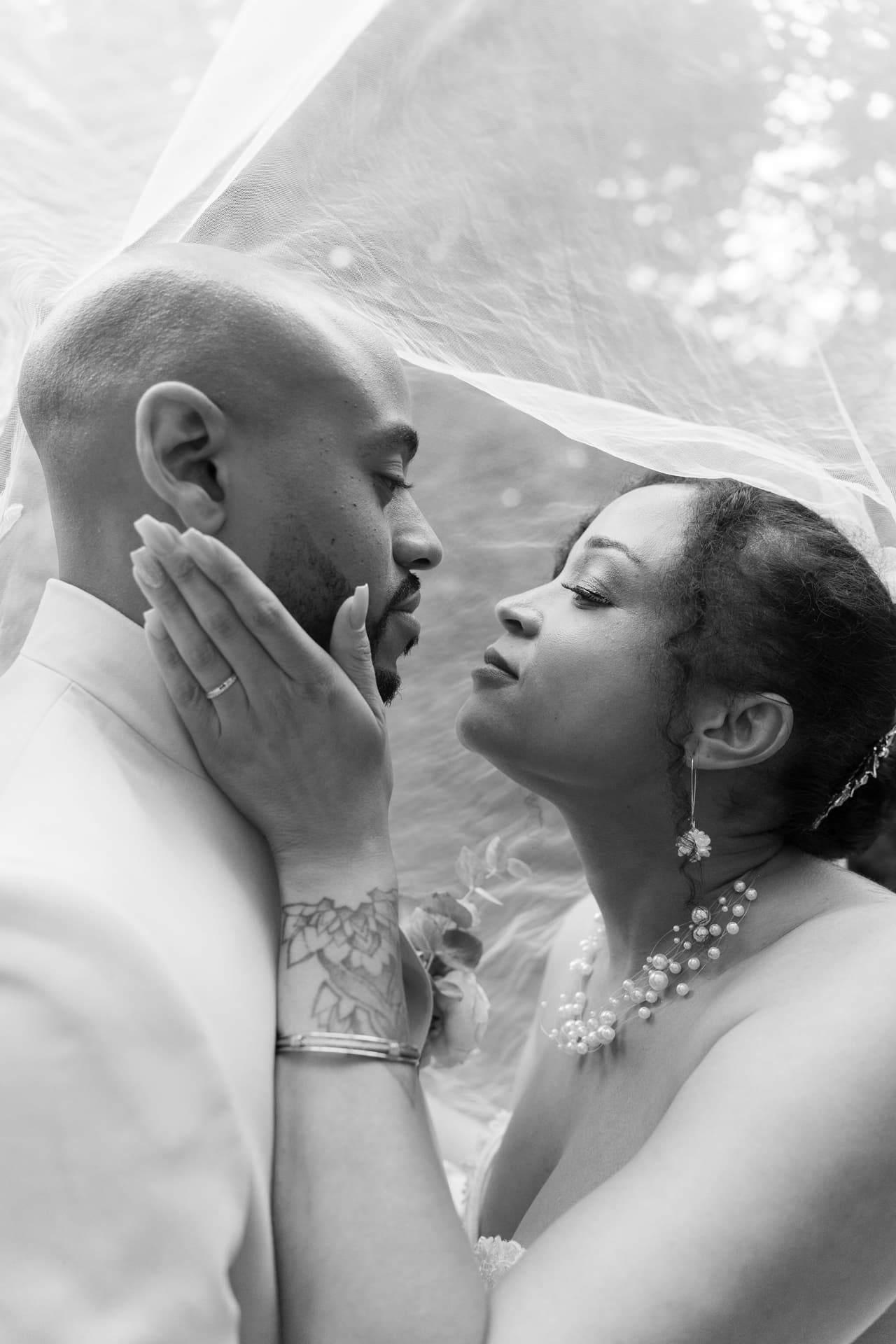 Les mariés se rapprochent sous le voile, photographiés en noir et blanc